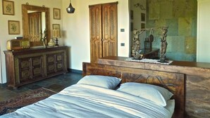 A bedroom with a wooden headboard, a large mirror, a dresser, and a bed with patterned bedding.