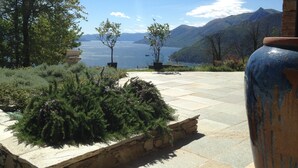 A patio with stone flooring, potted plants, and a view of a lake and mountains.