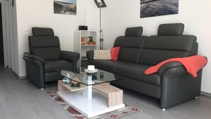 Un salon moderne avec une table basse en verre, deux canapés noirs et un plaid rouge.
