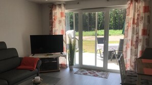 Un salon comprenant un canapé, une table basse, un téléviseur et une porte-fenêtre coulissante donnant sur un espace extérieur.