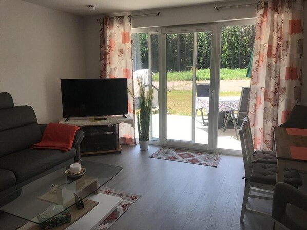 A living room with a sofa, a coffee table, a TV, and a sliding glass door leading to an outdoor area. - New quiet apartment in the coastal forest Graal-Müritz Apartment Zweisamkeit Hasenwinkel 4 ground floor<br> (Gelbensande)