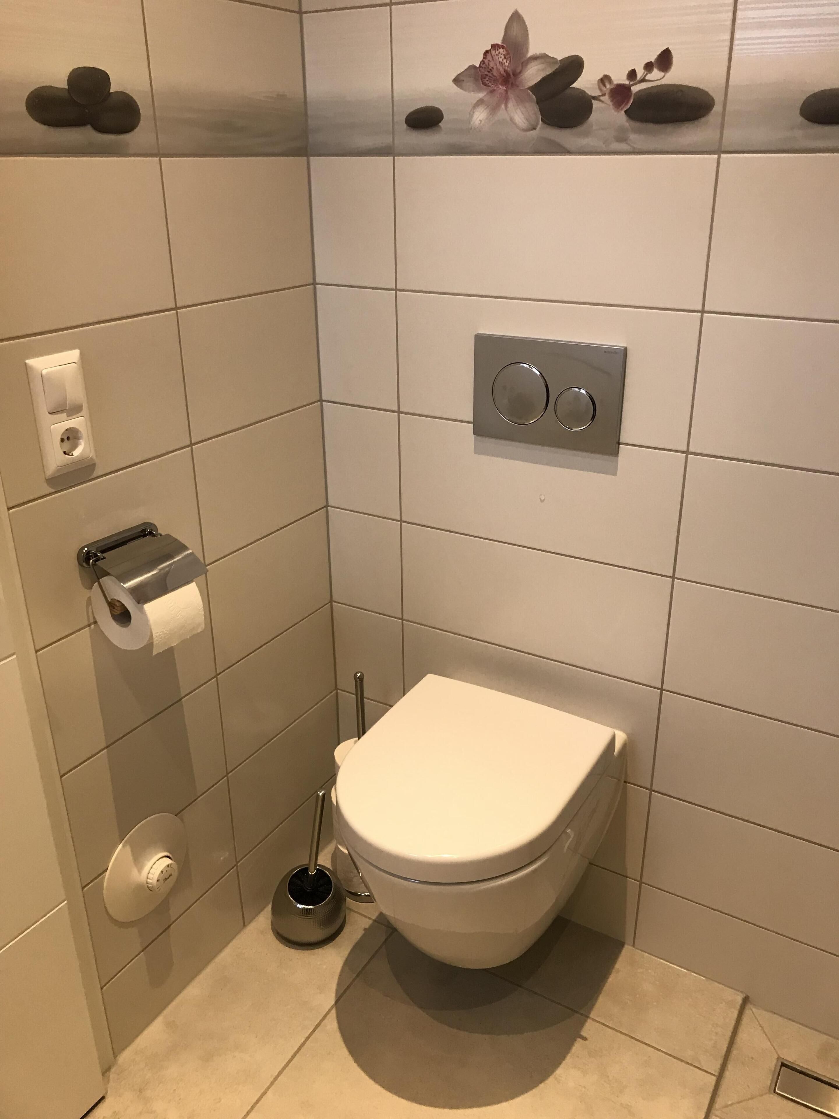 A modern bathroom with a toilet, a paper towel dispenser, a flush handle, and a bidet.