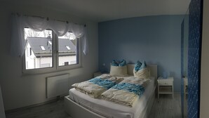 A bedroom with a bed, a window, a nightstand, and a door. - House Seewind Hohenfelden (Hohenfelden)