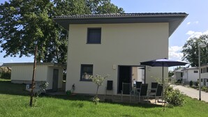 A two-story building with a flat roof, a small balcony, and a patio area with outdoor seating. - House Seewind Hohenfelden (Hohenfelden)