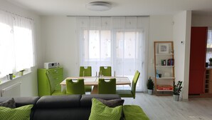 A modern living room with a green sofa, a dining table with chairs, a bookshelf, and a radiator. - House Seewind Hohenfelden (Hohenfelden)