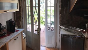 Une cuisine rustique avec un mur en pierre, un plafond en bois et une porte donnant sur l’extérieur.