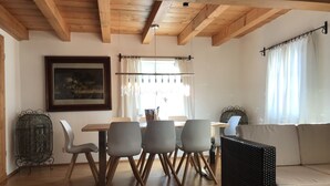Un coin repas avec une table et des chaises en bois, un canapé en osier noir et un tableau encadré au mur.
