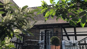 Un bâtiment traditionnel avec un toit en tuiles, un mur en pierre et une rambarde en métal noir.