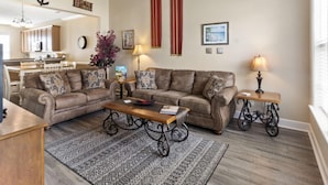 A spacious living room with a high ceiling, a staircase, and a kitchen in the background. - Egret Run #214 Beautiful Condo (North Myrtle Beach)