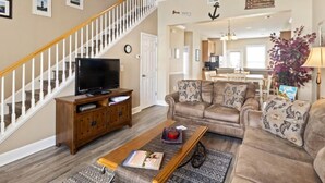 A spacious living room with a staircase, a television, a sofa, and a coffee table. - Egret Run #214 Beautiful Condo (North Myrtle Beach)