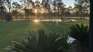 Un campo de golf con un estanque, árboles y un atardecer.