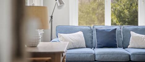 A room with a blue sofa, a lamp, and a view of greenery outside.