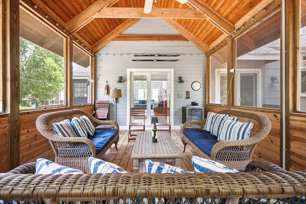 A covered porch with wicker furniture, a table, and a view of the house.