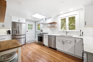 A modern kitchen with white cabinetry, stainless steel appliances, and a wooden floor.