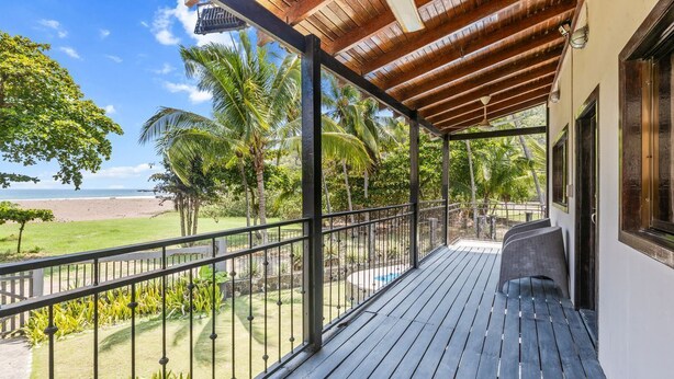 A wooden deck with a metal railing overlooking a beach and palm trees.