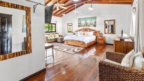 A spacious bedroom with a wooden ceiling, a large bed, a wooden dresser, and a wicker chair.