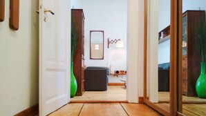 Un couloir au plancher de bois mène à une pièce où se trouvent un canapé, une petite table et un miroir accroché au mur.