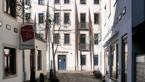 Une rue pavée bordée de bâtiments des deux côtés, une enseigne indiquant « UR. Galerie d’art textile et d’artisanat », et une porte bleue.