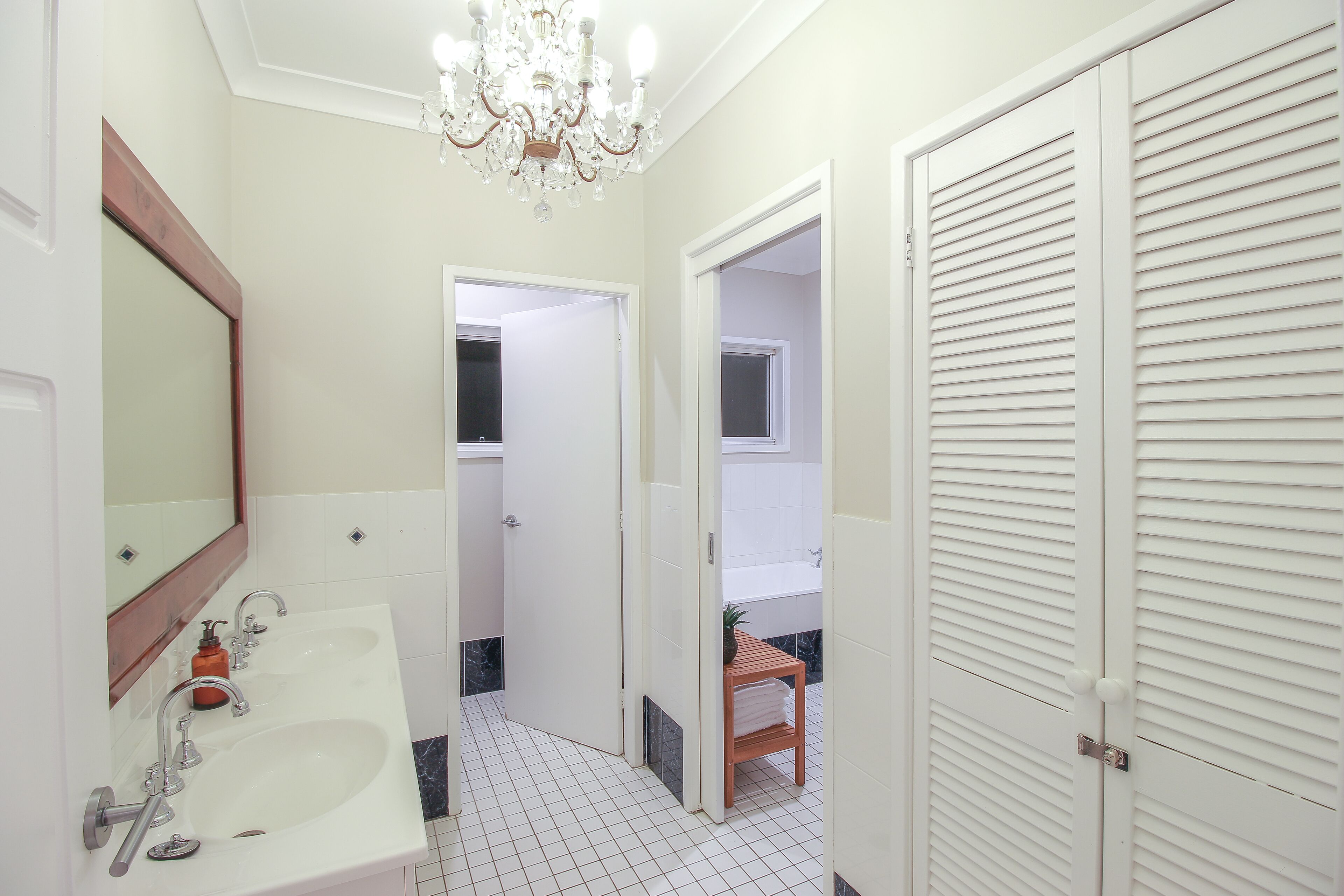 Een badkamer met een wastafel, spiegel, kroonluchter en een deur naar de douche.