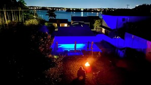 A nighttime view of a waterfront property with a pool, a patio area, and a view of the water and distant buildings.