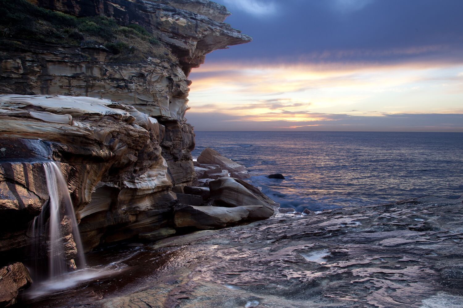 A coastal landscape with a waterfall, rocky cliffs, and the ocean.