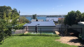 A residential area with a view of a body of water, houses, and a fenced yard with a pool.