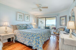 A bedroom with a large bed, a ceiling fan, wicker furniture, and framed artwork on the walls. - CRC 1302 - Beautiful Oceanfront Condo with Amazing Views (St Augustine)