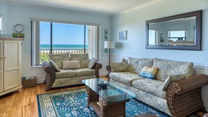 A living room with a view of the ocean, wicker furniture, and a large mirror. - CRC 1302 - Beautiful Oceanfront Condo with Amazing Views (St Augustine)