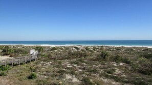 A beach with a wooden walkway leading to a small structure, surrounded by dunes and sparse vegetation. - CRC 1302 - Beautiful Oceanfront Condo with Amazing Views (St Augustine)