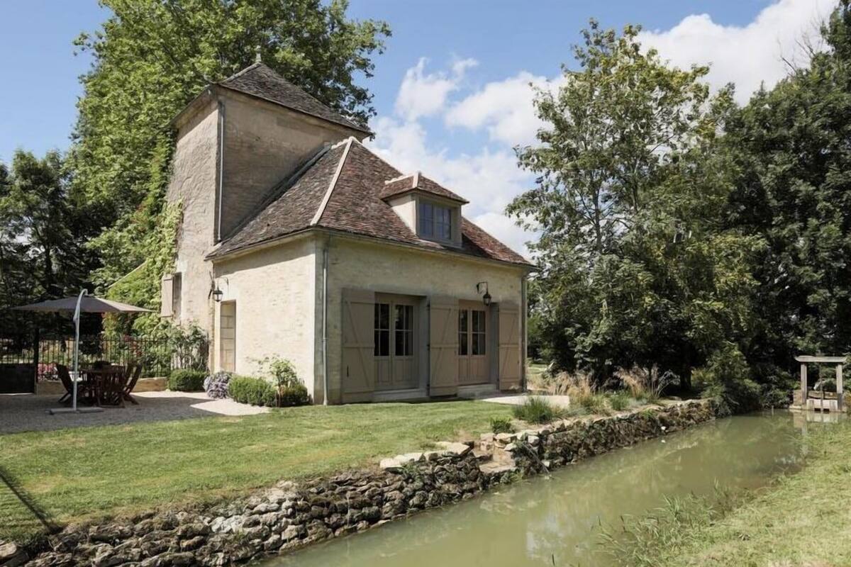 Uma casa de dois andares com fachada de pedra, telhado inclinado e um pequeno jardim com lago.