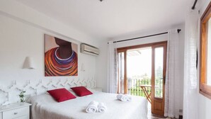 Ein Schlafzimmer mit einem Bett, roten Kissen, einem Gemälde, einer Klimaanlage, einem Fenster mit Vorhängen und einem Balkon.