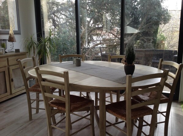 Une table de salle à manger ronde, entourée de six chaises en bois, un pot de fleurs et une petite lampe de table.
