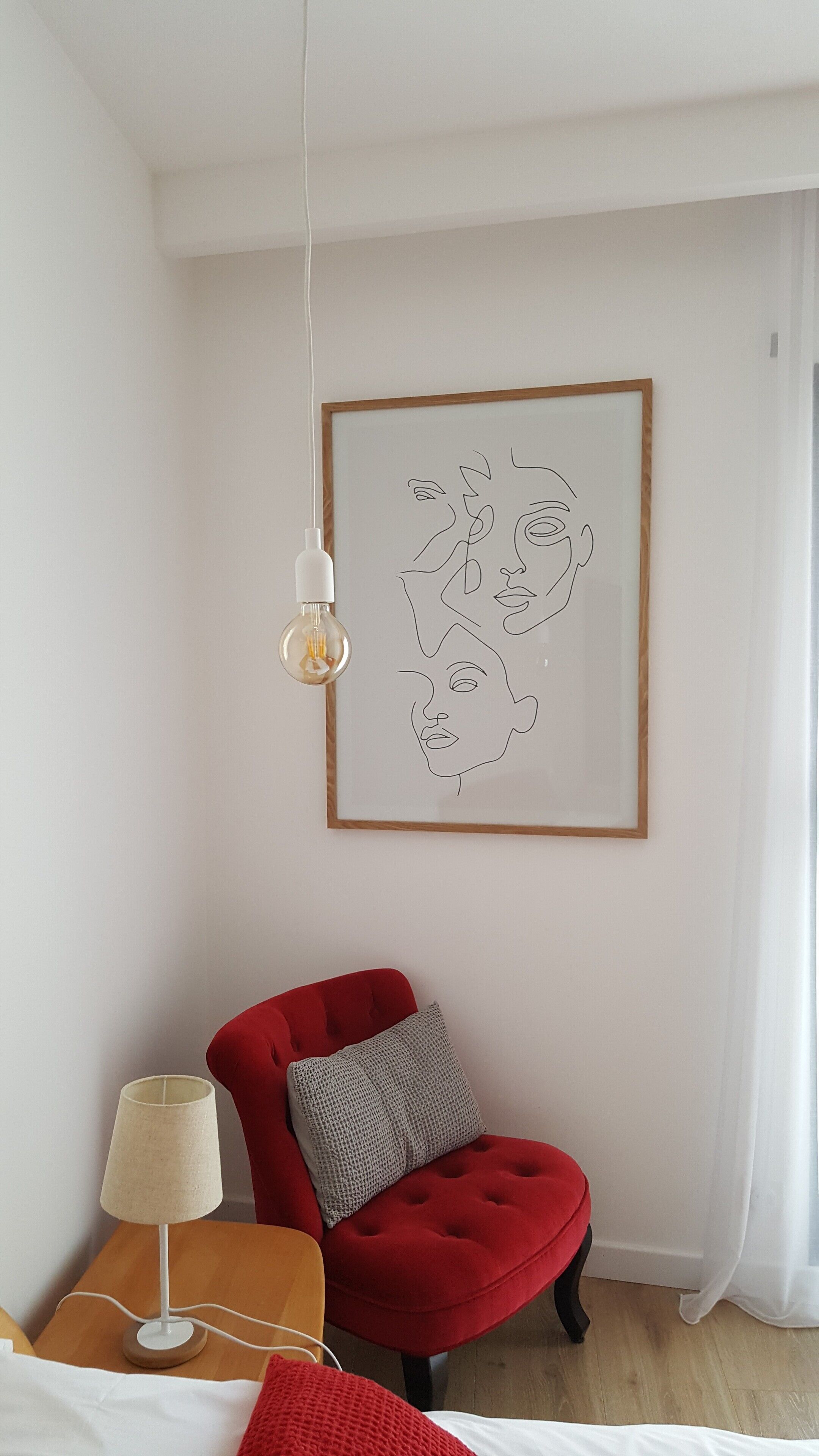 A modern room with a red chair, a lamp, and a framed abstract artwork on the wall.