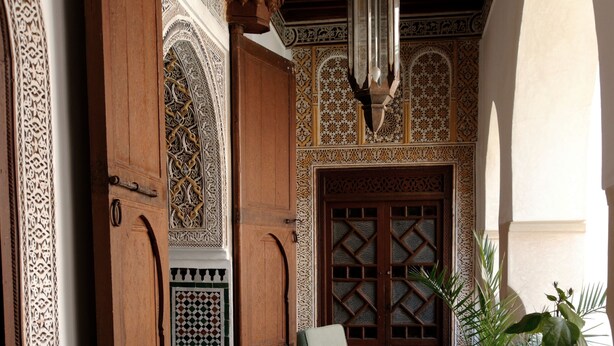 An interior courtyard with a checkered floor, wooden furniture, and intricate wall designs.
