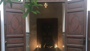 An open wooden door with intricate carvings, leading to a room with a patterned floor and a decorative ceiling light.