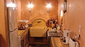 A narrow kitchen with a herringbone floor pattern, a wooden cabinet with a checkered backsplash, and a refrigerator on the left.
