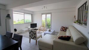Ein geräumiges Wohnzimmer mit großem Fenster, Flachbildfernseher, Sofa und Essbereich.