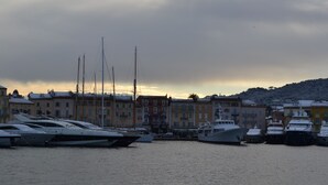 Ein Yachthafen mit mehreren dort angestückten Yachten, umgeben von Gebäuden mit Balkonen und einer hügeligen Landschaft im Hintergrund.