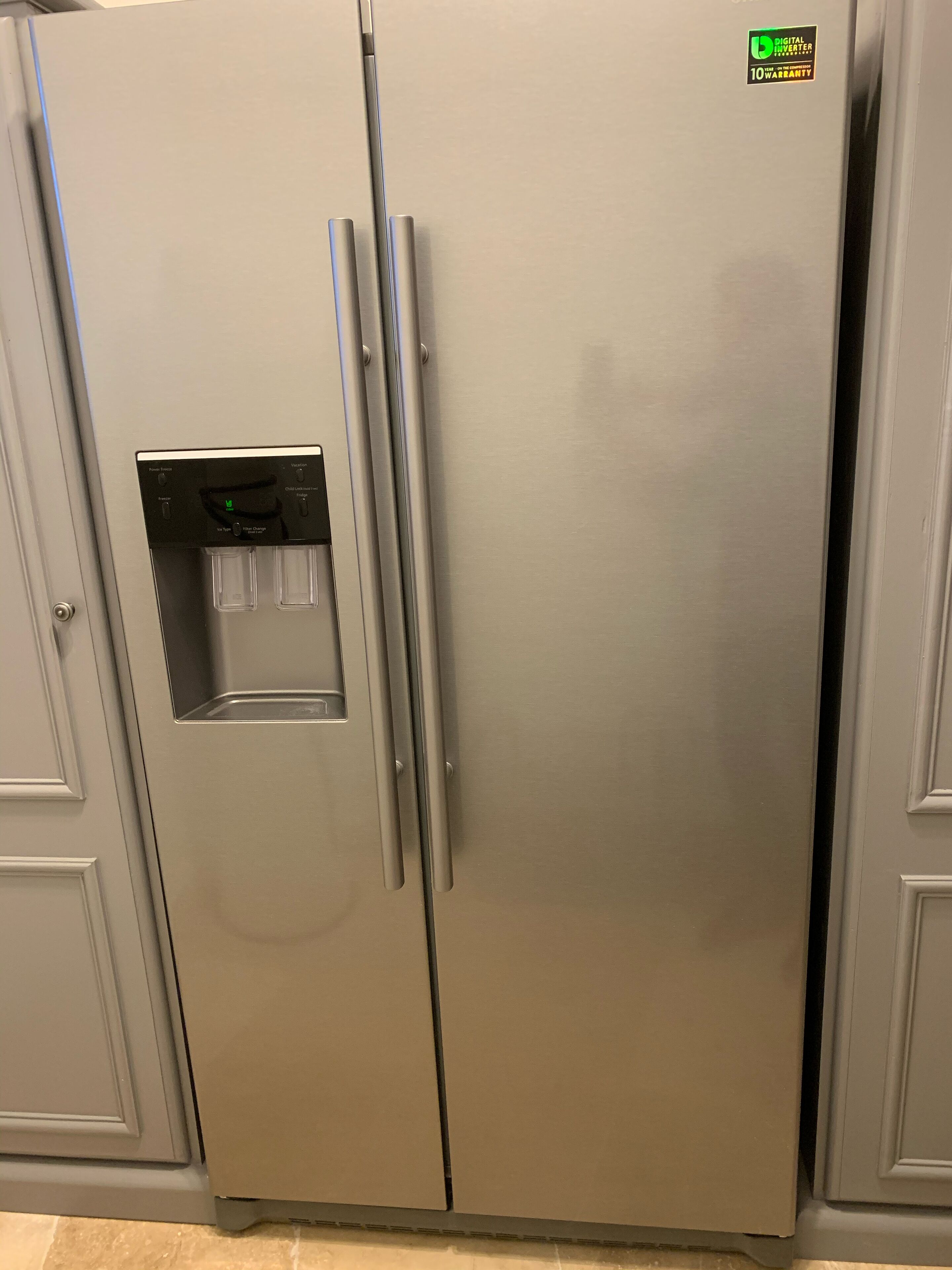 A stainless steel refrigerator with a water dispenser, a digital inverter, and a 10-year warranty sticker.