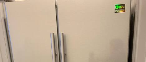 A stainless steel refrigerator with a water dispenser, a digital inverter, and a 10-year warranty sticker.