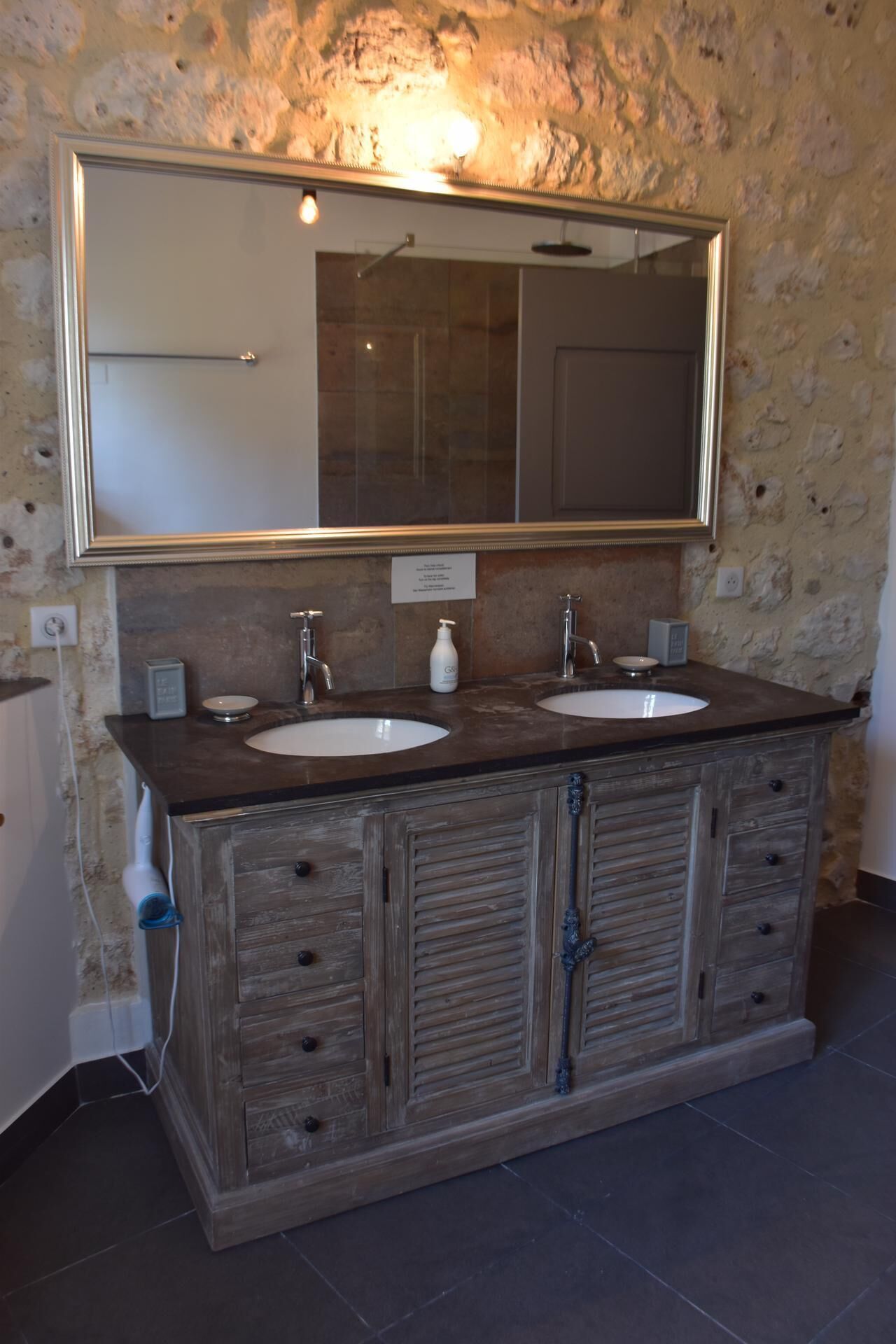 A bathroom with a double sink vanity, a large mirror, and a stone wall.