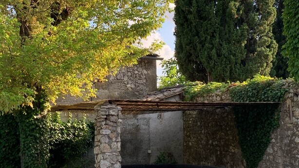 A stone structure with a built-in seating area, surrounded by greenery and trees.