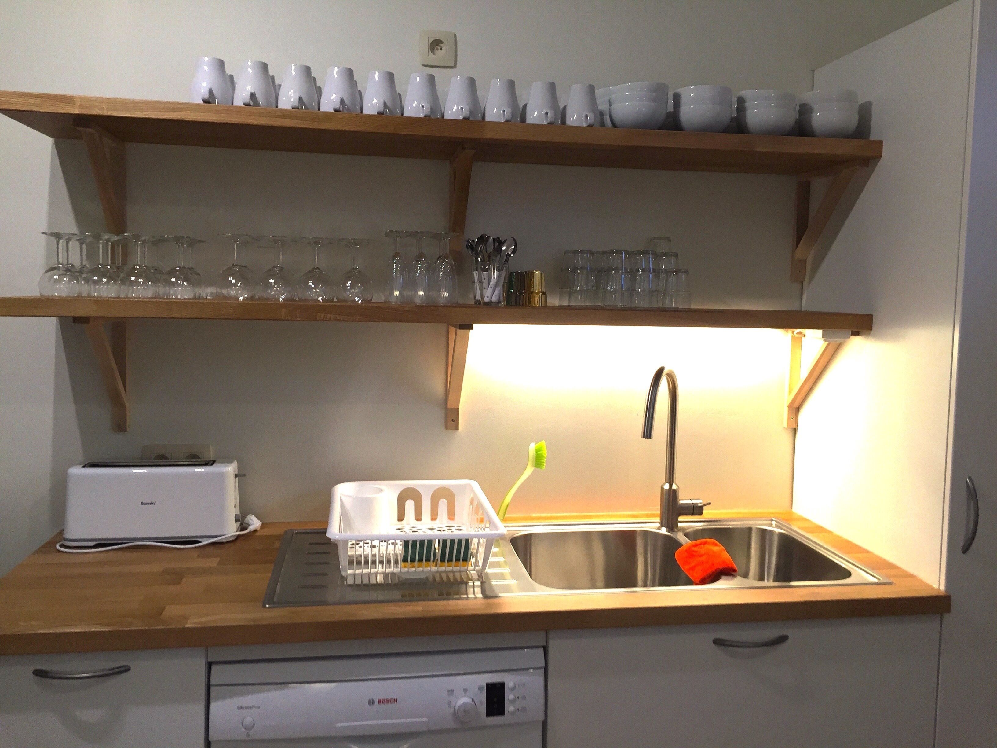 Une cuisine équipée d’un lave-vaisselle Bosch, d’un évier avec un robinet et d’étagères au-dessus pour ranger les tasses et les verres.