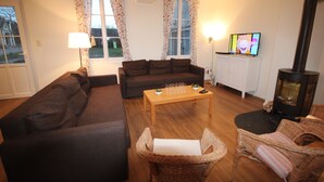 Ein gemütliches Wohnzimmer mit einer Couch, einem Korbsessel, einem Holztisch und einem Fernseher.