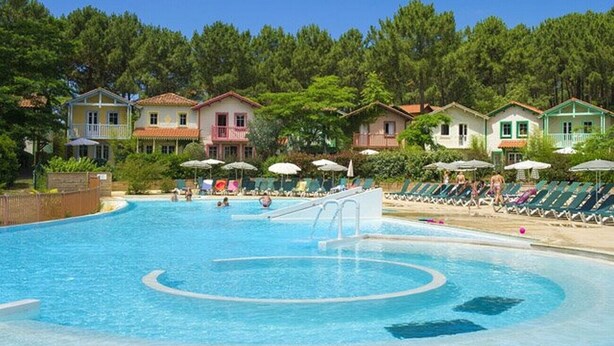 A swimming pool with lounge chairs and umbrellas, surrounded by buildings with balconies.