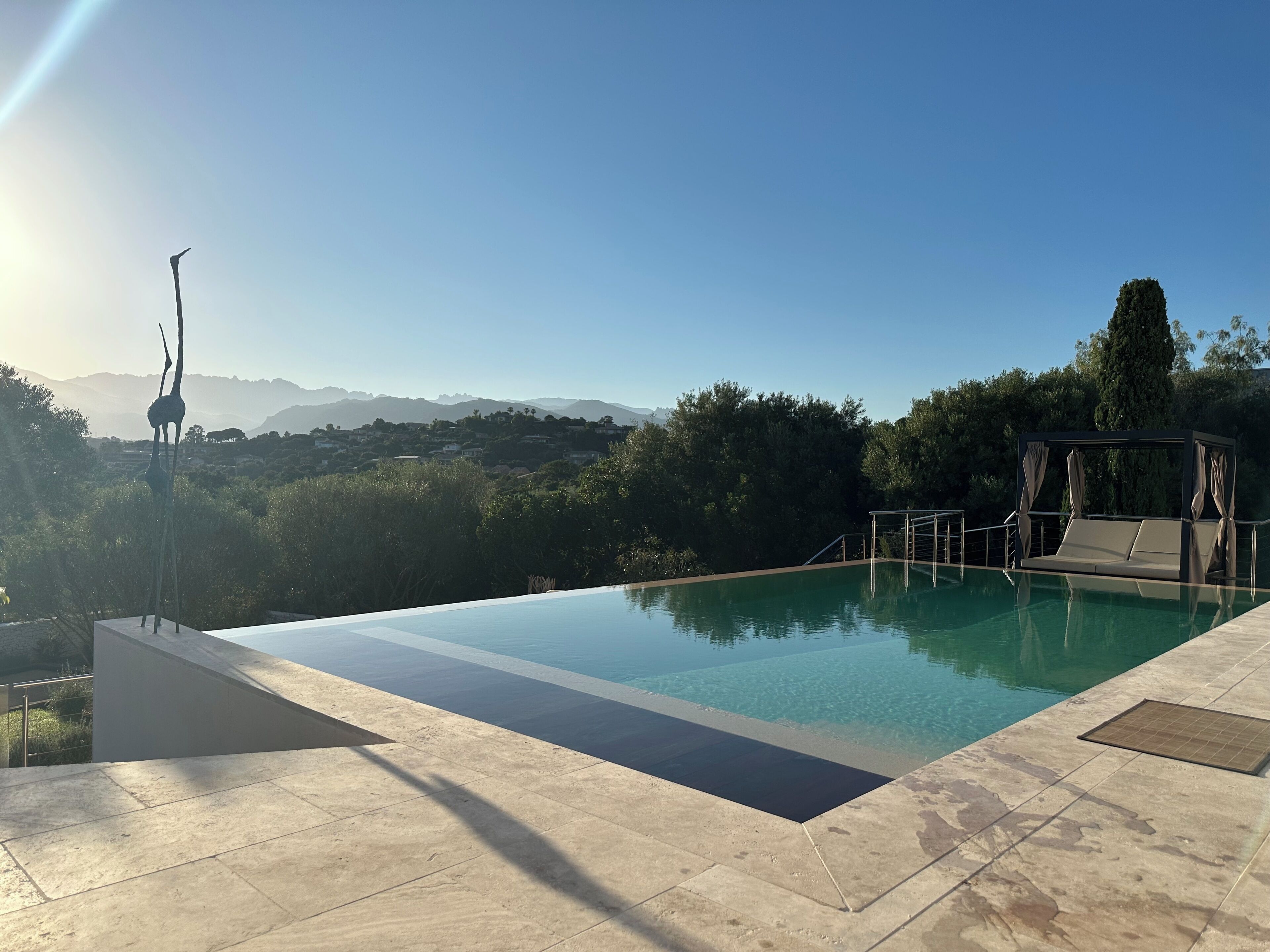 A clear blue swimming pool with a view of distant mountains, a pergola, and a well-maintained patio area.