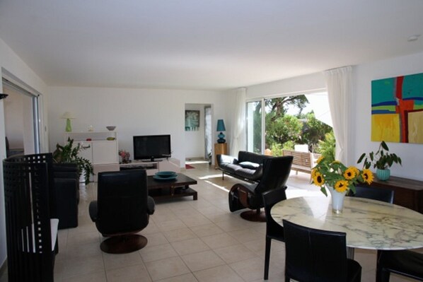 Un salon moderne avec un canapé, des fauteuils, un téléviseur et une table à manger décorée de tournesols.