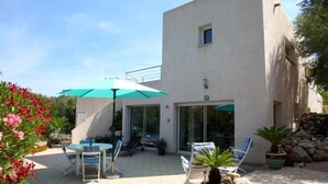 Un pati exterior modern amb taula i cadires, un parasol verd i plantes en testos.