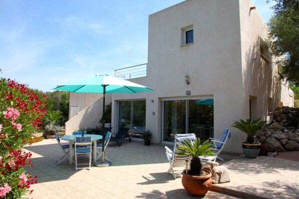Une terrasse extérieure moderne, avec une table et des chaises, un parasol vert et des plantes en pot.