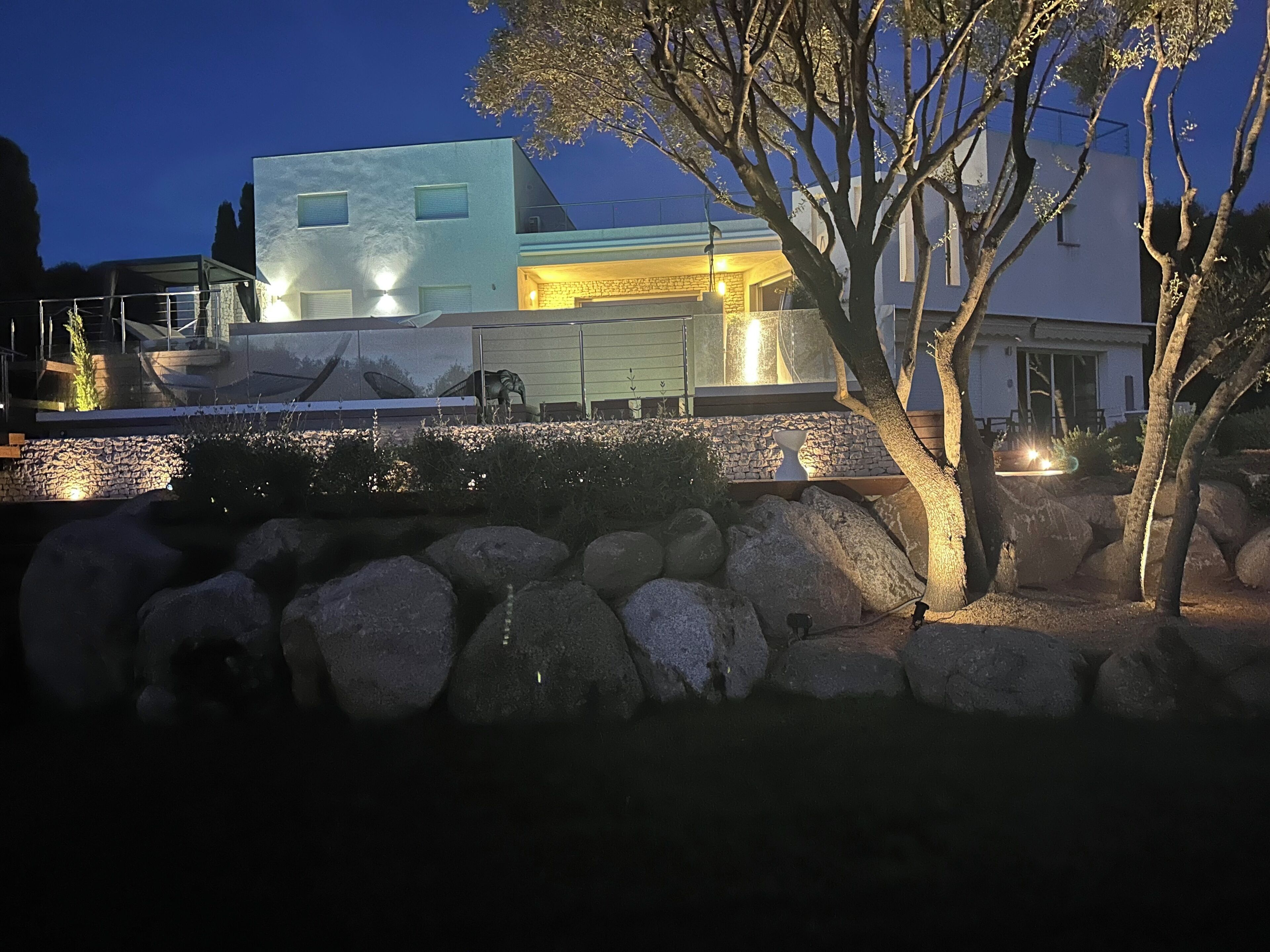 A modern house with a stone wall and a tree in the foreground.